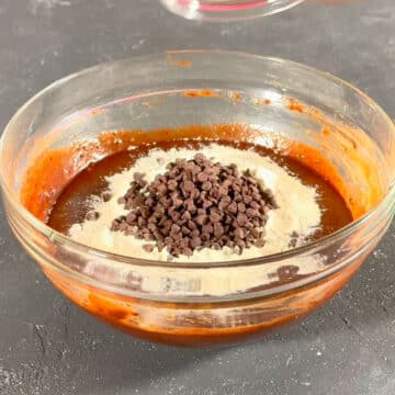 Flour and chocolate chips adds to chocolate mixture in glass bowl. 