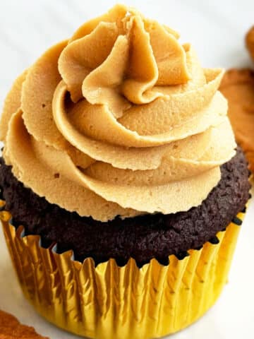 Easy Biscoff Cupcakes With Cookie Butter Frosting in Golden Liners on White Marble Background.