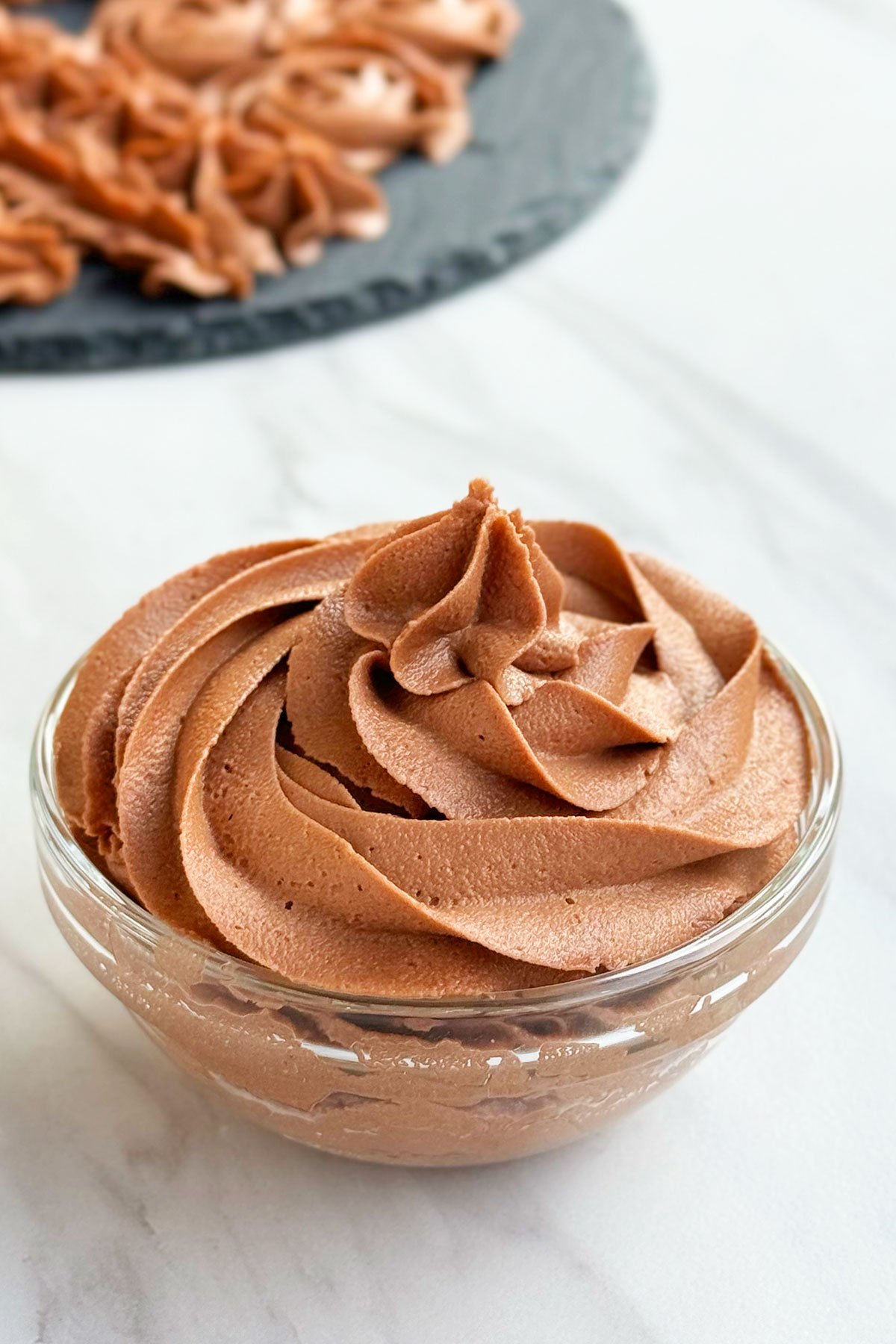 Glass Bowl Full of Nutella Frosting on White Marble Background.