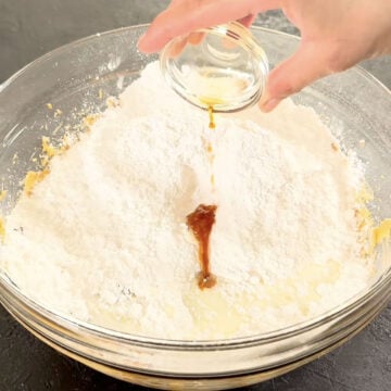 Powdered sugar, milk and vanilla being added to glass bowl. 