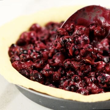 Blueberry filling being spooned into a prepared crust. 