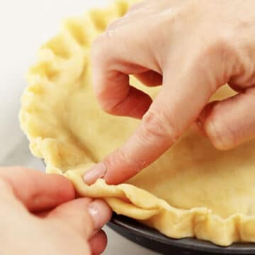 Pie crust edges being crimped with fingers and thumbs. 