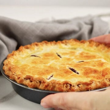 Baked golden brown pie being served on white marble with gray napkin. 