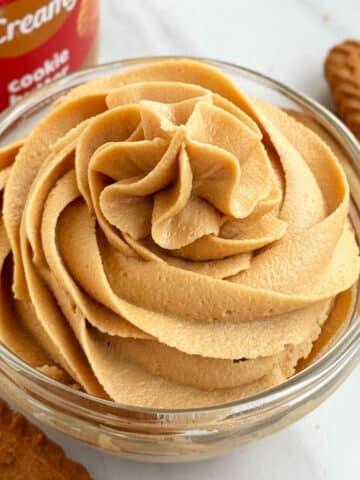 Glass Bowl of Biscoff Frosting on White Marble Background.