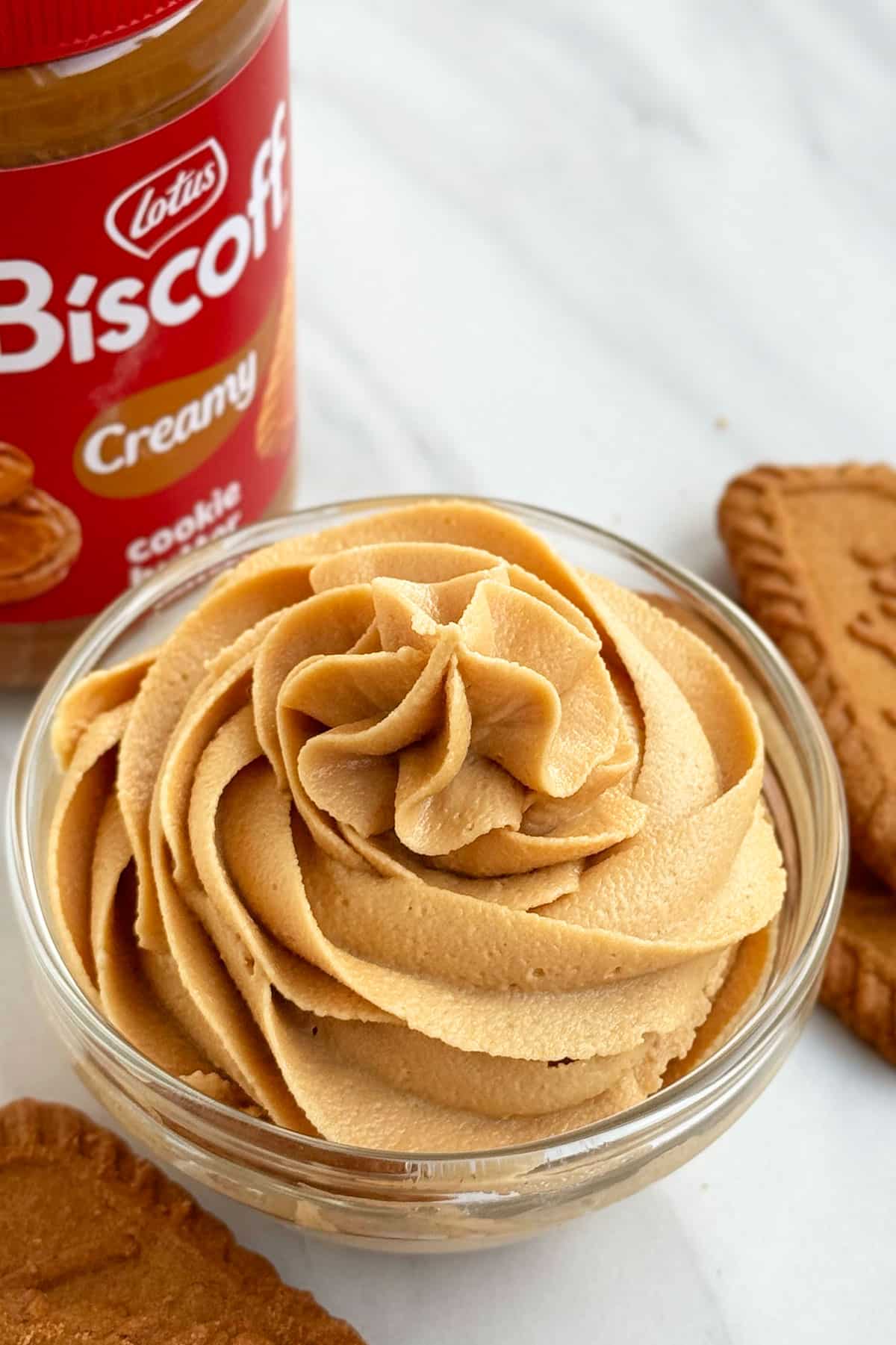 Easy Biscoff Frosting in Glass Bowl With Jar of Biscoff Spread and Lotus Cookies in Background.