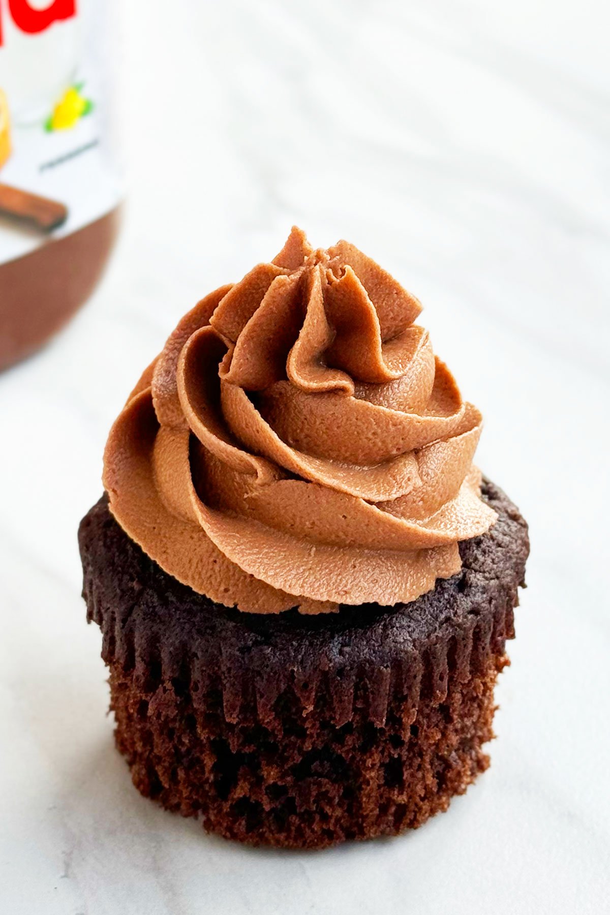 Frosted Chocolate Hazelnut Cupcakes With Liner Removed on White Marble Background. 
