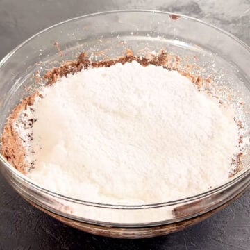 Powdered sugar in glass bowl of Nutella and butter mixture. 