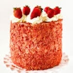 Layered Strawberry Crunch Cake With Cake Mix Box Covered in Buttercream Frosting and Crunchy Topping and Fresh Strawberries on White Dish.