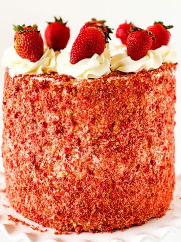 Layered Strawberry Crunch Cake With Cake Mix Box Covered in Buttercream Frosting and Crunchy Topping and Fresh Strawberries on White Dish.