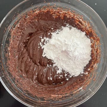 Powdered sugar and meringue powder added to chocolate mixture in glass bowl. 