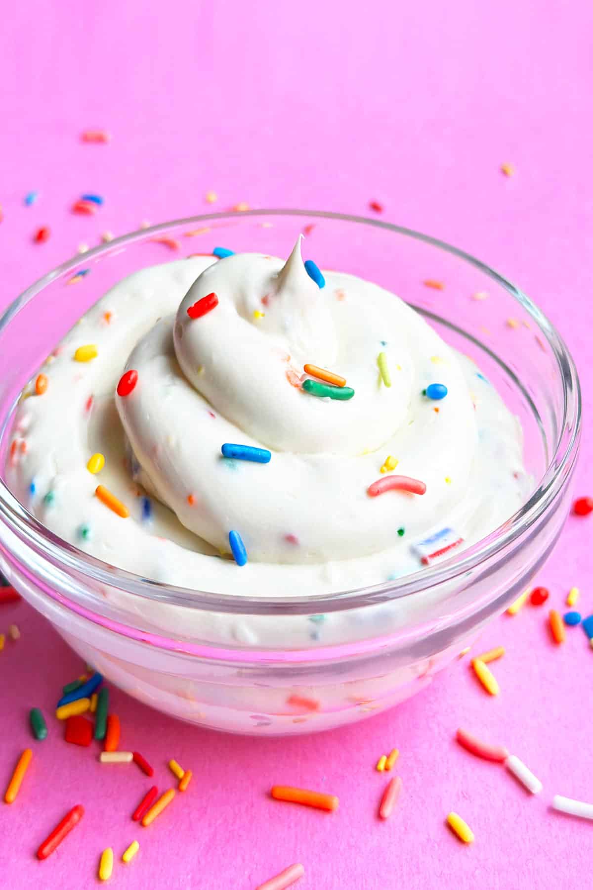 Glass Bowl of Cake Batter Dip Topped With Colorful Sprinkles on Pink Background. 