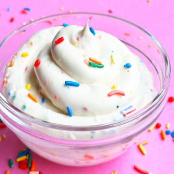 Glass Bowl of Funfetti Cake Batter Dip Topped With Colorful Sprinkles on Pink Background.