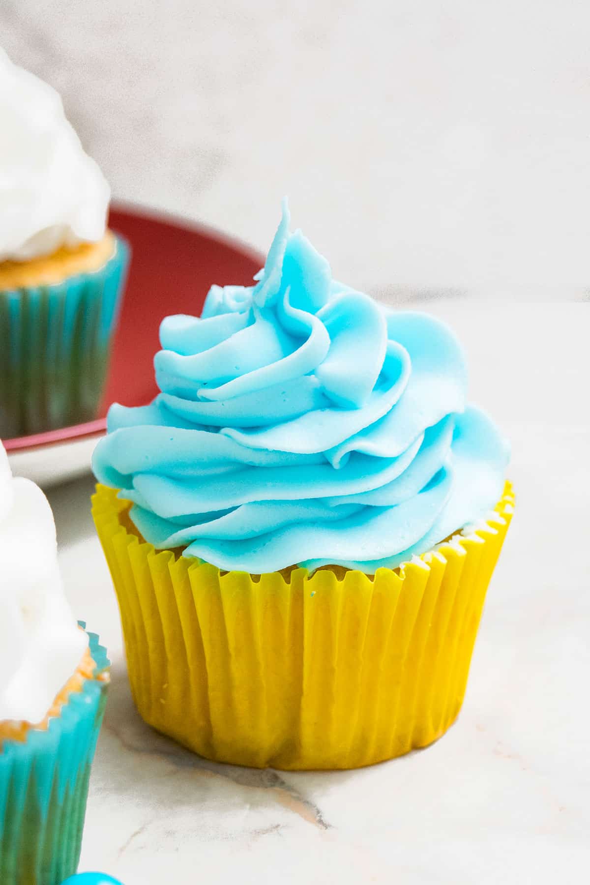 Blue icing swirled on top of cupcake in yellow liner. 