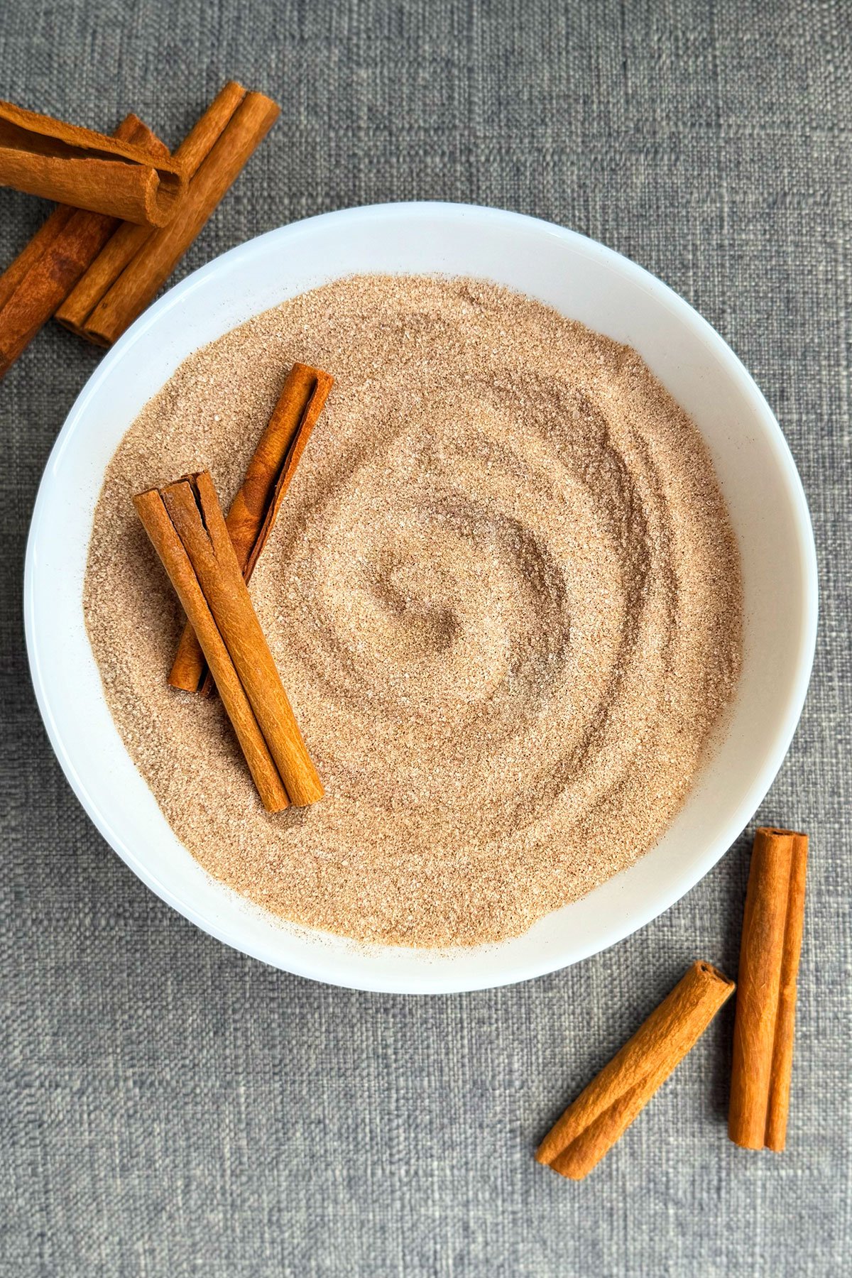 Easy Homemade Cinnamon Sugar in White Bowl With Cinnamon Sticks on Gray Background. 