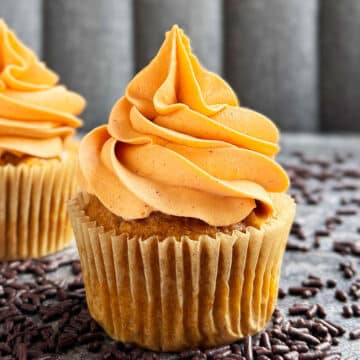 Easy Soft Pumpkin Cupcakes With Spiced Cream Cheese Frosting on Rustic Gray Background With Chocolate Sprinkles Scattered Everywhere.