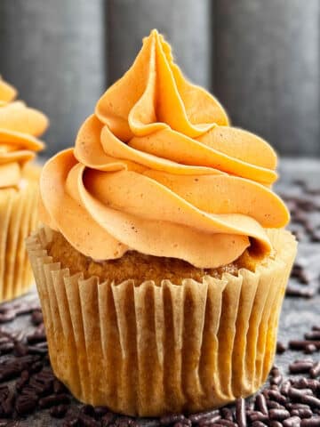 Easy Soft Pumpkin Cupcakes With Spiced Cream Cheese Frosting on Rustic Gray Background With Chocolate Sprinkles Scattered Everywhere.