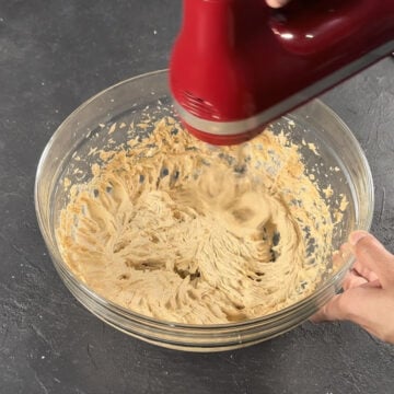 Ingredients being mixed together in glass bowl with red hand held mixer. 