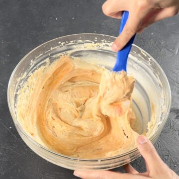 Orange food coloring added to mixture and is being mixed with a blue spatula. 