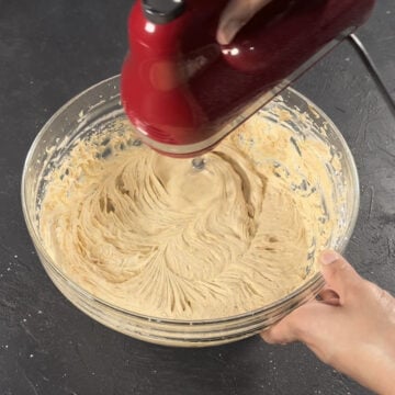 Smooth icing being mixed together with red hand held mixer. 