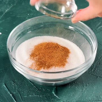 Ground cinnamon being added to other ingredient in glass bowl. 