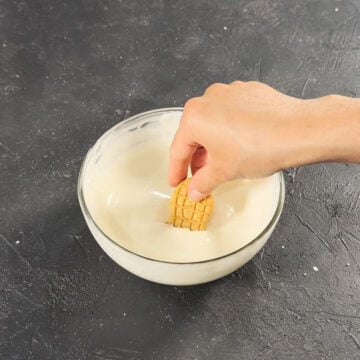 Cookie being dipped in glass bowl of melted white chocolate. 