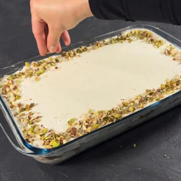 Chopped pistachios being sprinkled on top of frosted cake. 