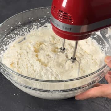 Mascarpone filling being whipped in a glass bowl with hand held mixer. 