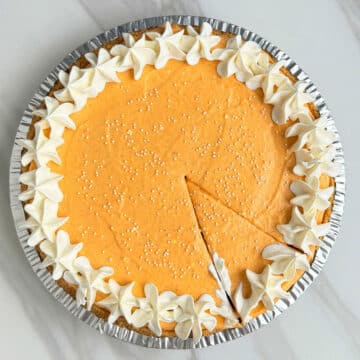 Easy No Bake Pumpkin Pie on White Marble Background With a Slice Cut Out.