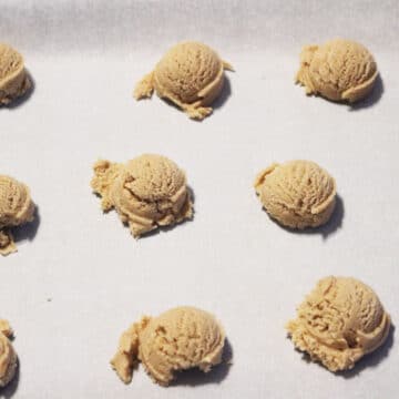 Rough cookie dough balls dropped onto a baking tray with white parchment paper. 