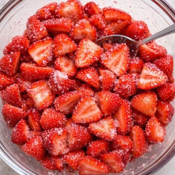 Sugar and strawberries mixed together in glass bowl. 