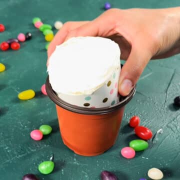 Frosted cupcake being added to a mini plastic flower pot. 