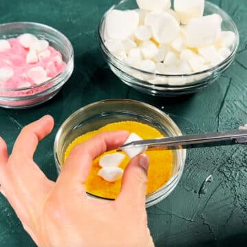 Mini marshmallows being cut with scissors diagonally. 
