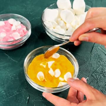 Marshmallows being coated in a bowl of colored sugar. 