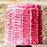 Decorated Pink Buttercream Ruffle Cake on Cake Stand with Brick Background.