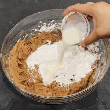 Additional powdered sugar and milk being added in glass bowl of icing.