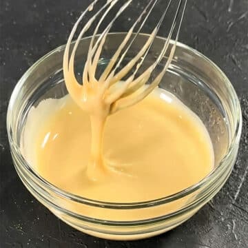 Glass Bowl Filled With Easy Maple Glaze Drizzle Icing and Stainless Steel Whisk on Rustic Gray Background.