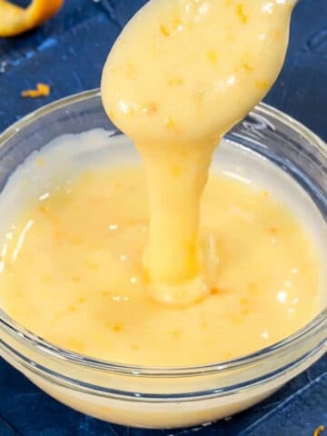 Spoonful of easy orange glaze drizzle icing for cake being poured in a glass bowl.