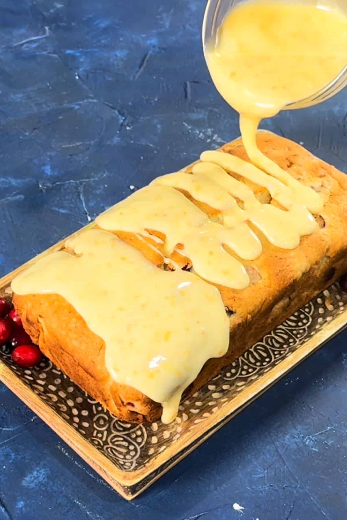 Orange drizzle icing being poured on top of of loaf cake. 