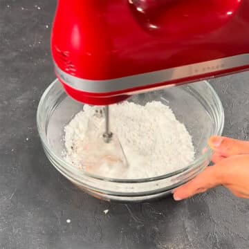 Ingredients being mixed together in glass bowl with hand held mixer. 