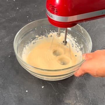 Ingredients being mixed together smoothly in bowl with red hand held mixer.  