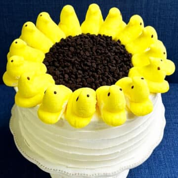 Easy Simple Sunflower Cake Decorated With Buttercream Frosting, Peeps Marshmallows and Chocolate Chips on White Cake Stand.