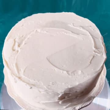 Filled and frosted cake on white cake stand. 