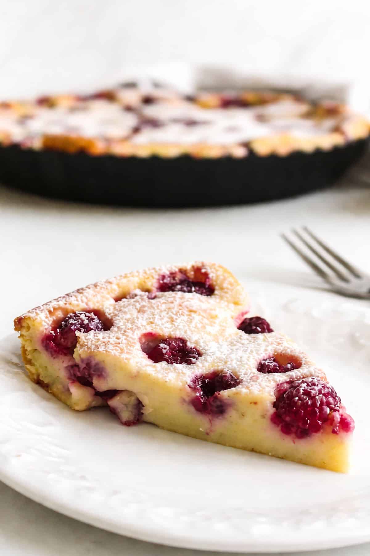 Slice of baked French custard cake dessert on white dish with fork. 