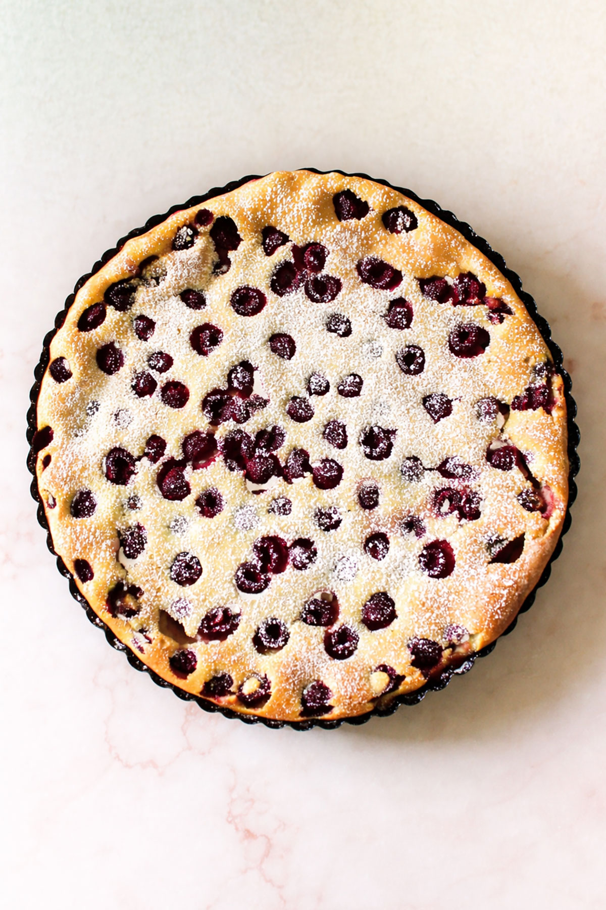 Easy French Clafoutis With Dusting of Powdered Sugar on Marble Background. 