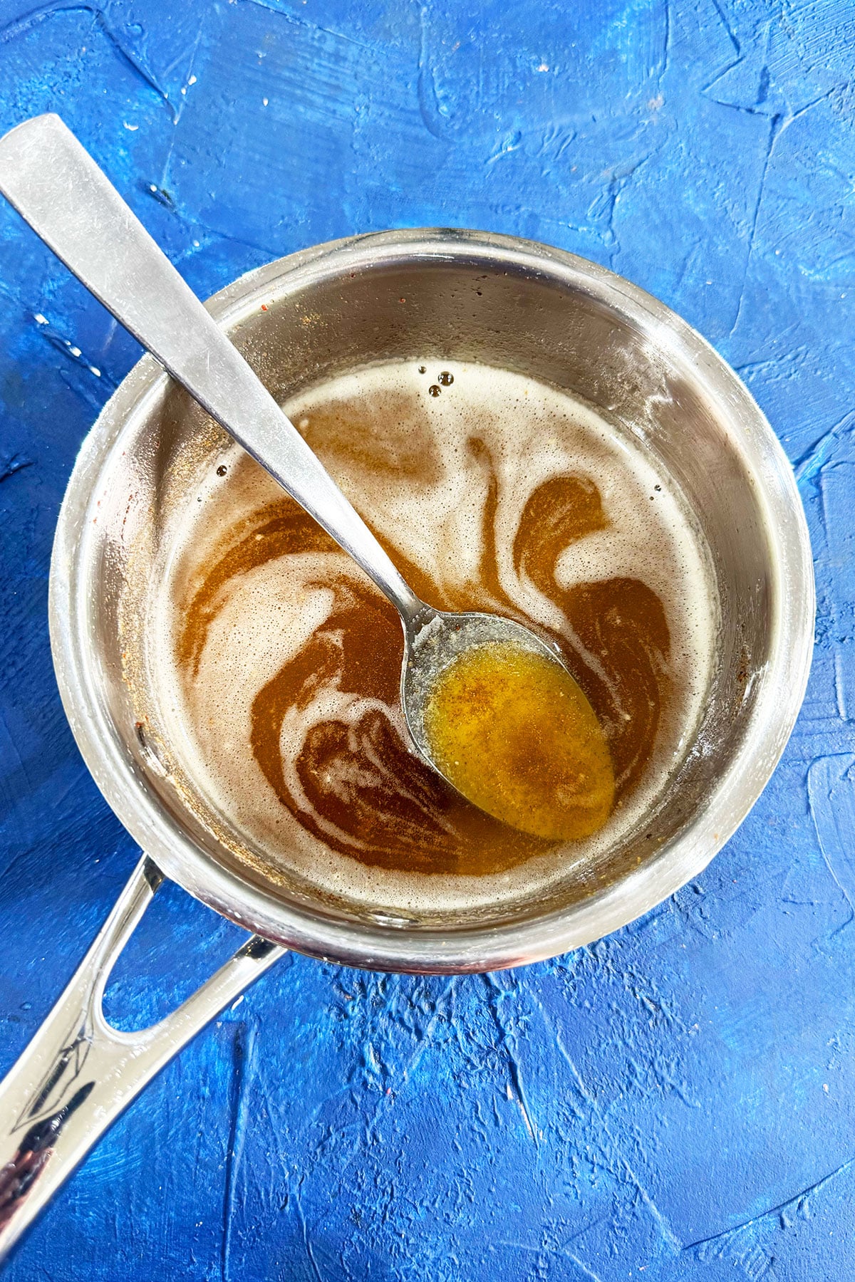 Cooked butter in stainless steel saucepan on blue background- Overhead shot. 