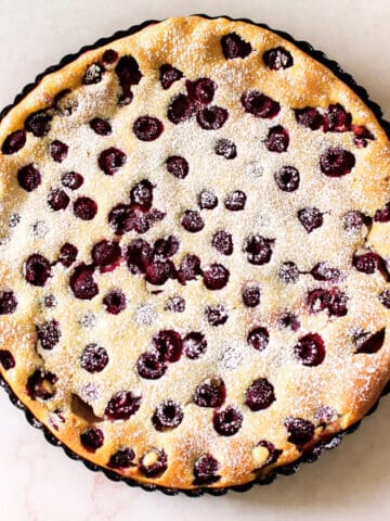 Easy French Clafoutis Dessert With Cherries and Raspberries and Dusting of Powdered Sugar on Marble Background- Overhead Shot.