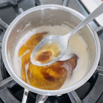 Closeup of spoonful of cooked brown milk solid flecks. 