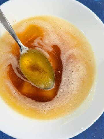 White bowl filled with homemade brown butter and spoon on blue background.
