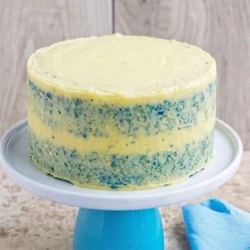 Semi frosted cake with thin layer of yellow frosting on stand.